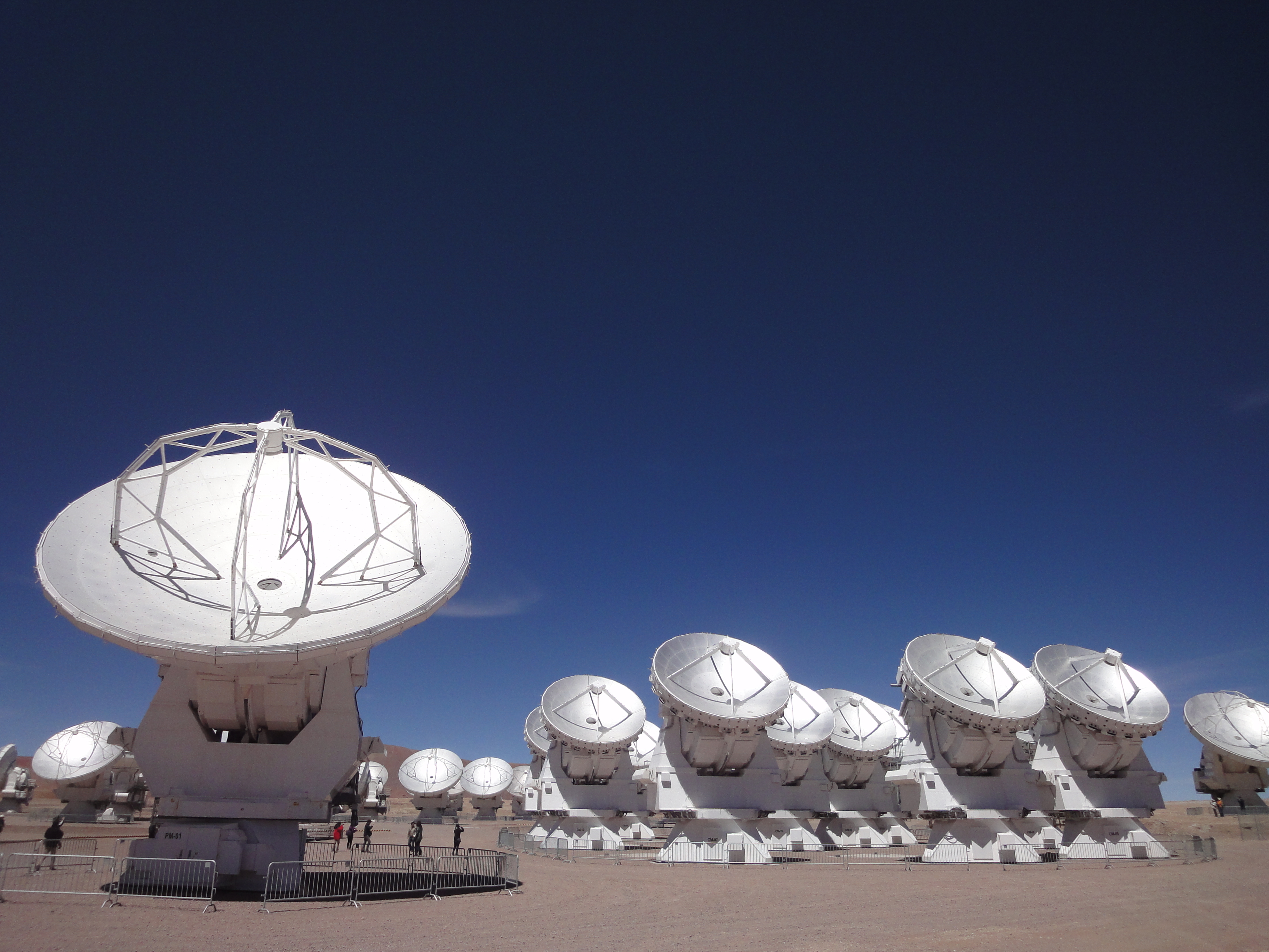 Several silver dish antennas pointing upwards to a dark blue sky
