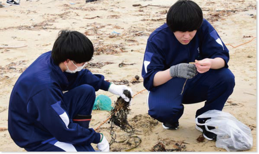 砂浜で漂着物を採取する2人の高校生