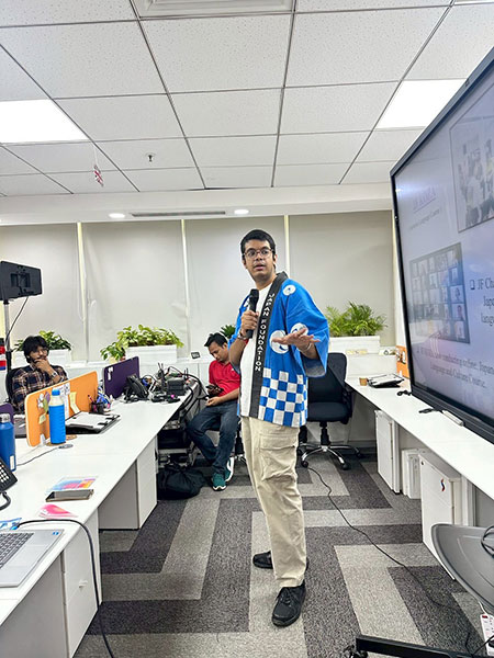 A Japan Foundation staff member introducing materials for learning the Japanese language, delivering an engaging presentation wearing a traditional attire, the “happi”.