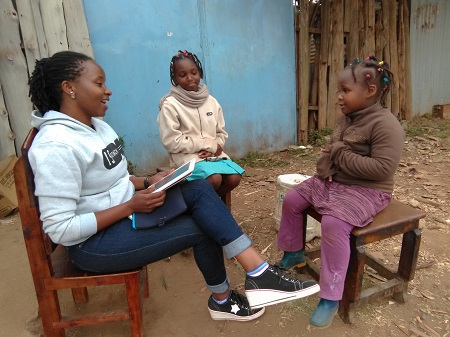 One adult researcher and two child interviewees sit on chairs outside talking.