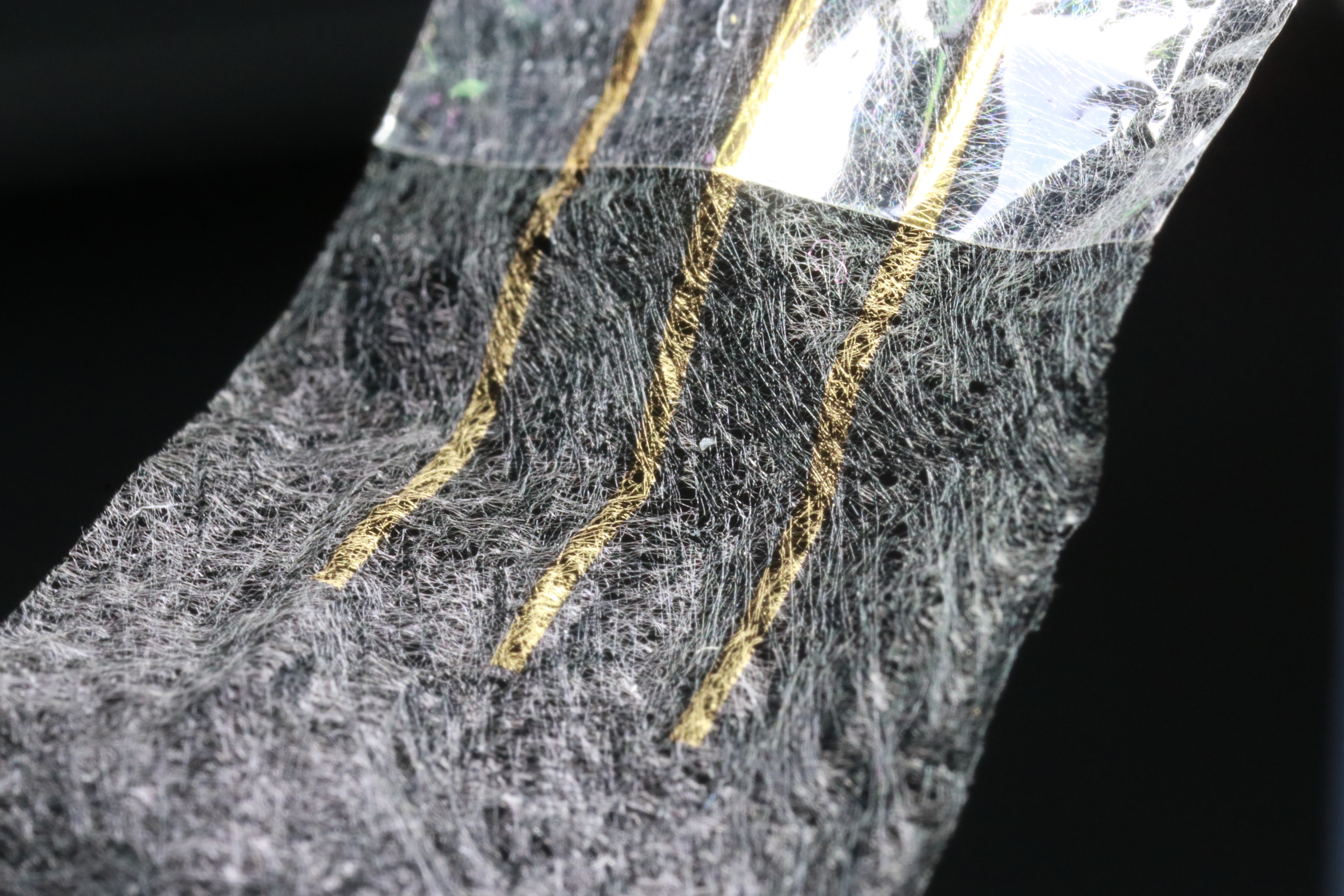 A thin white mesh of fibers on a black background. Small areas of the mesh are colored gold.