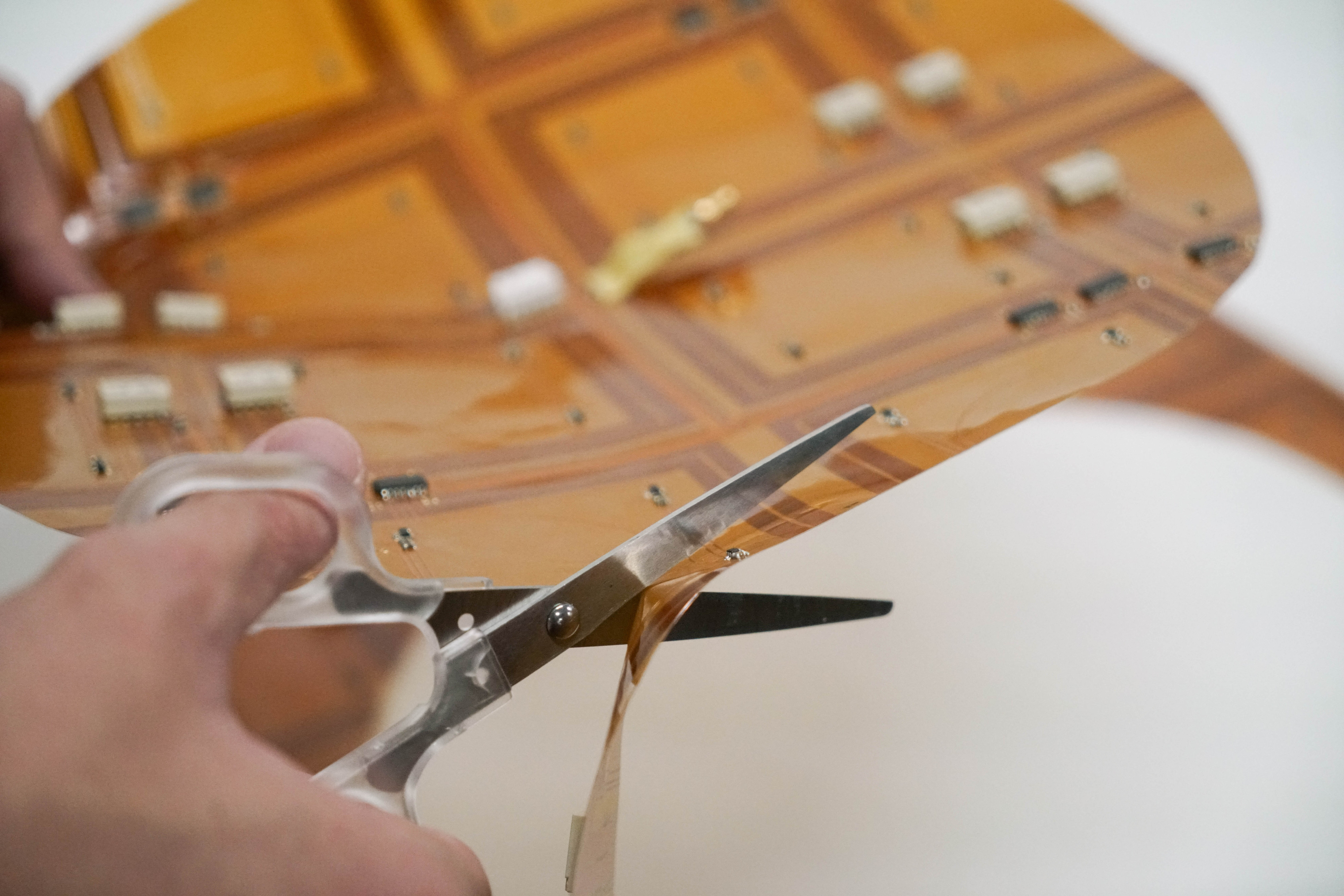 A hand holds a pair of scissors which are cutting an orange sheet