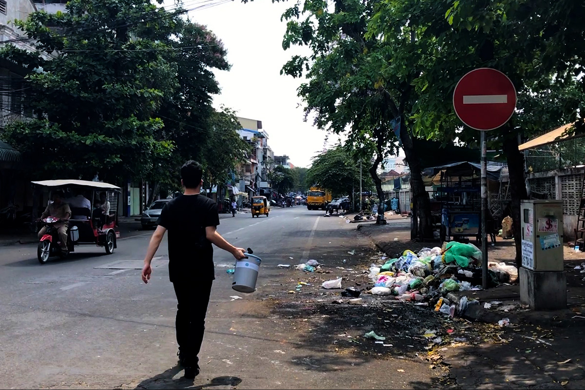 A man walks along in a road in Phnom Penh, Cambodia, while a tuk-tuck passes in the opposite direction.