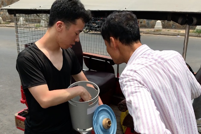Two men look into a Grubin bin while standing in front of a tuk-tuk, a Cambodian taxi.