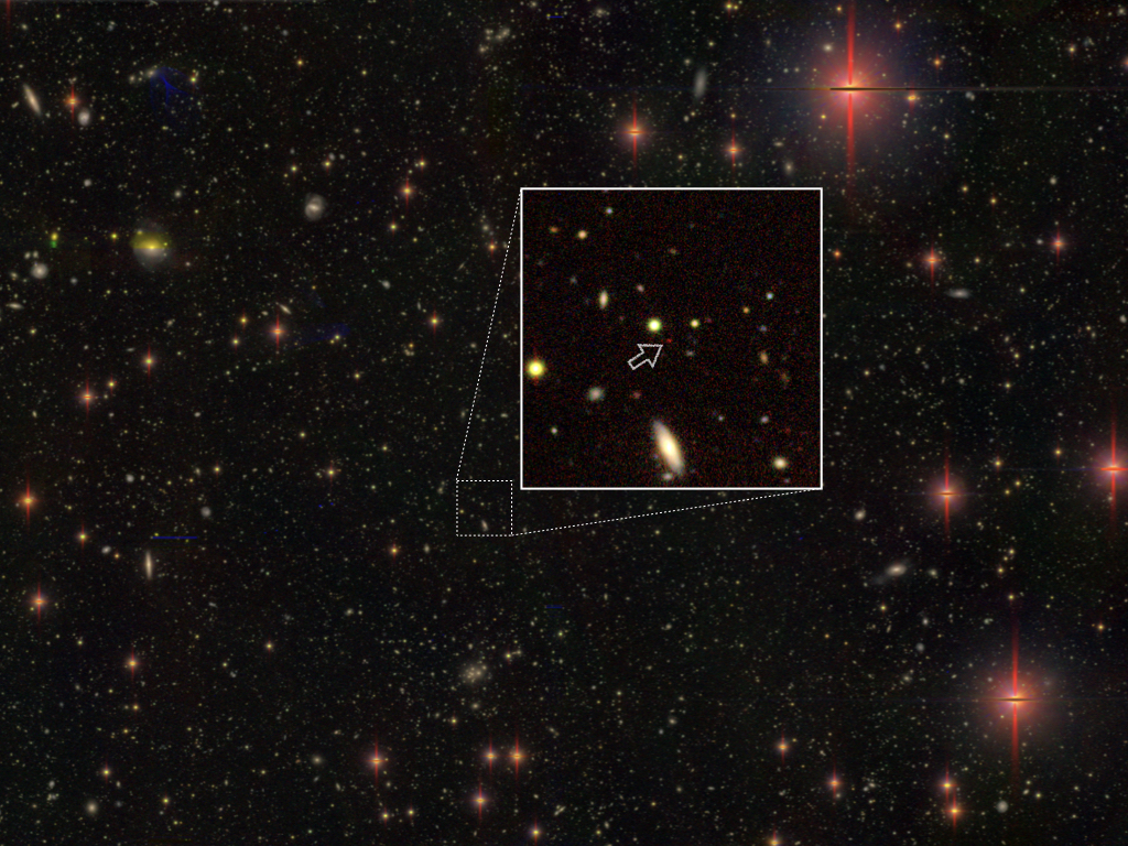 A black void sprinkled with coloured dots. A thin white square magnifies a part of the starfield image. Within, a small arrow points to a single red dot.