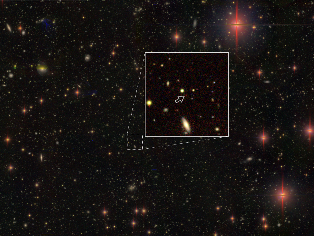 A black void sprinkled with coloured dots. A thin white square magnifies a part of the starfield image. Within, a small arrow points to a single red dot.