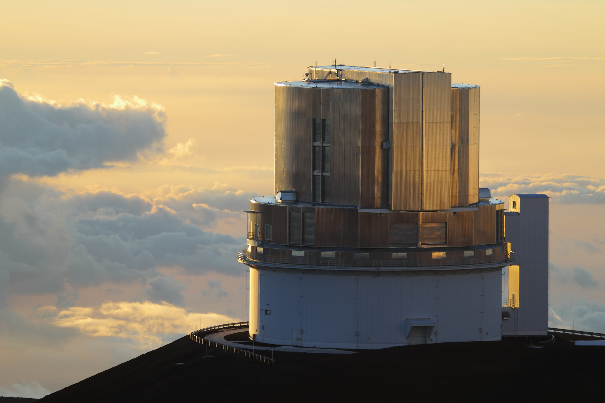 A white and gold cylindrical building is set against a sea of orange clouds at sunset.