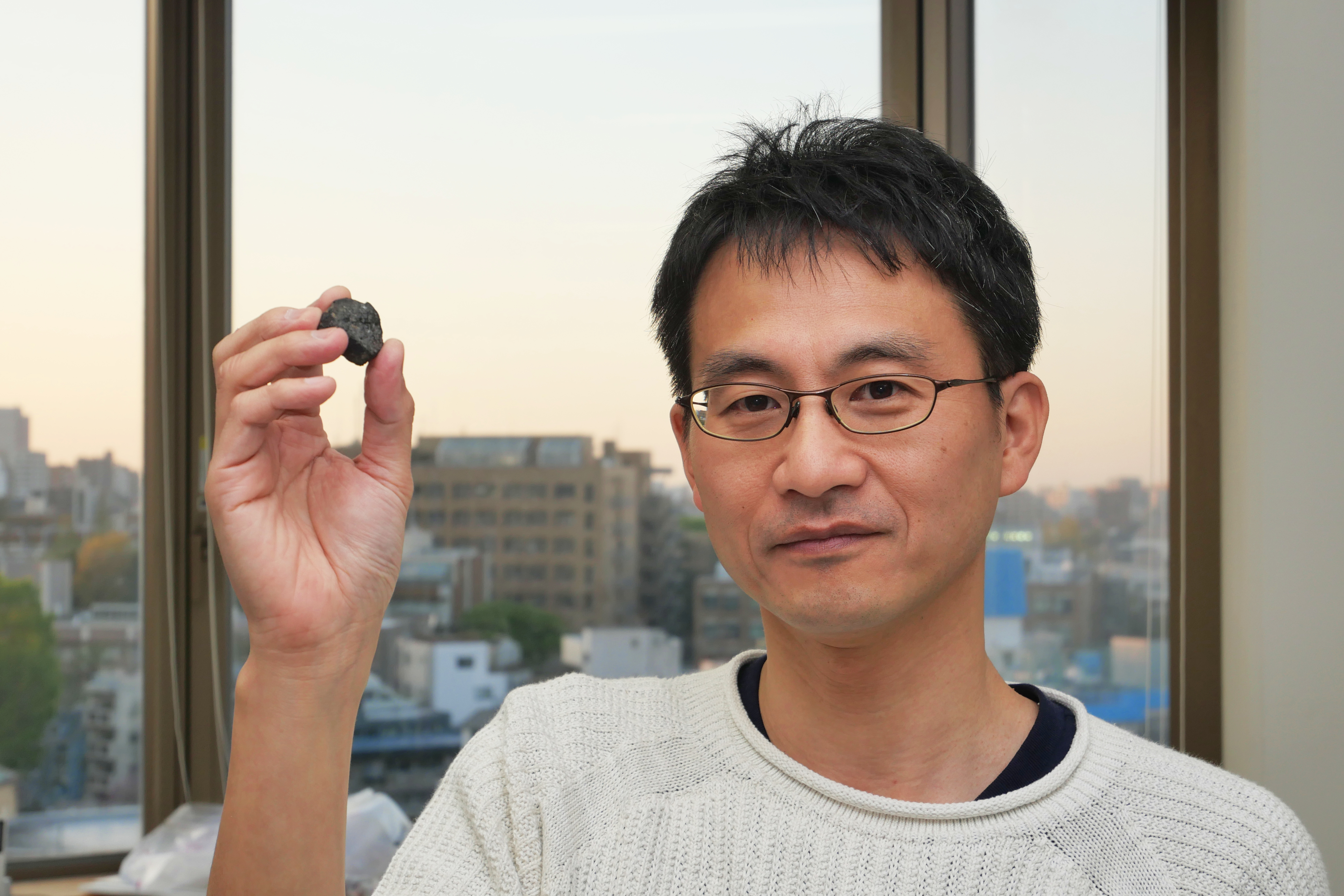 Portrait photo. Man on the right holding a small rock. The background is sunset over a cityscape.