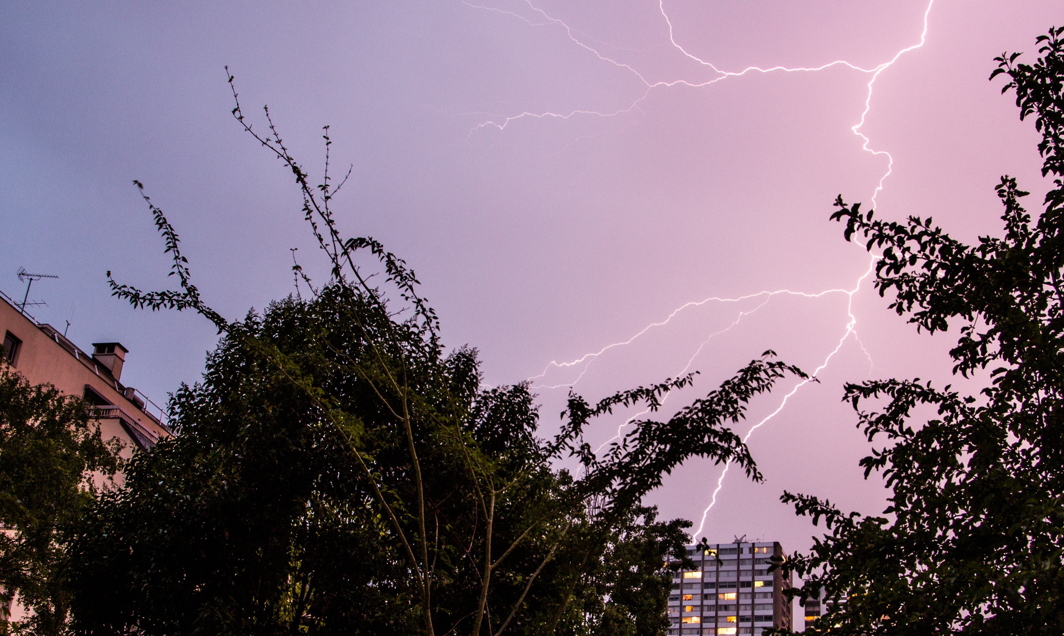 Lightning bolt across a dark sky with some buildings in the foreground.