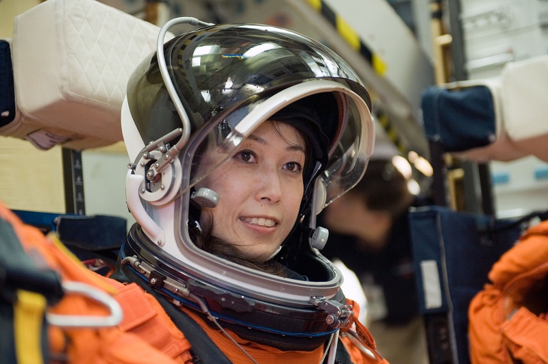 Naoko Yamazaki wears an orange space suit while sitting down.