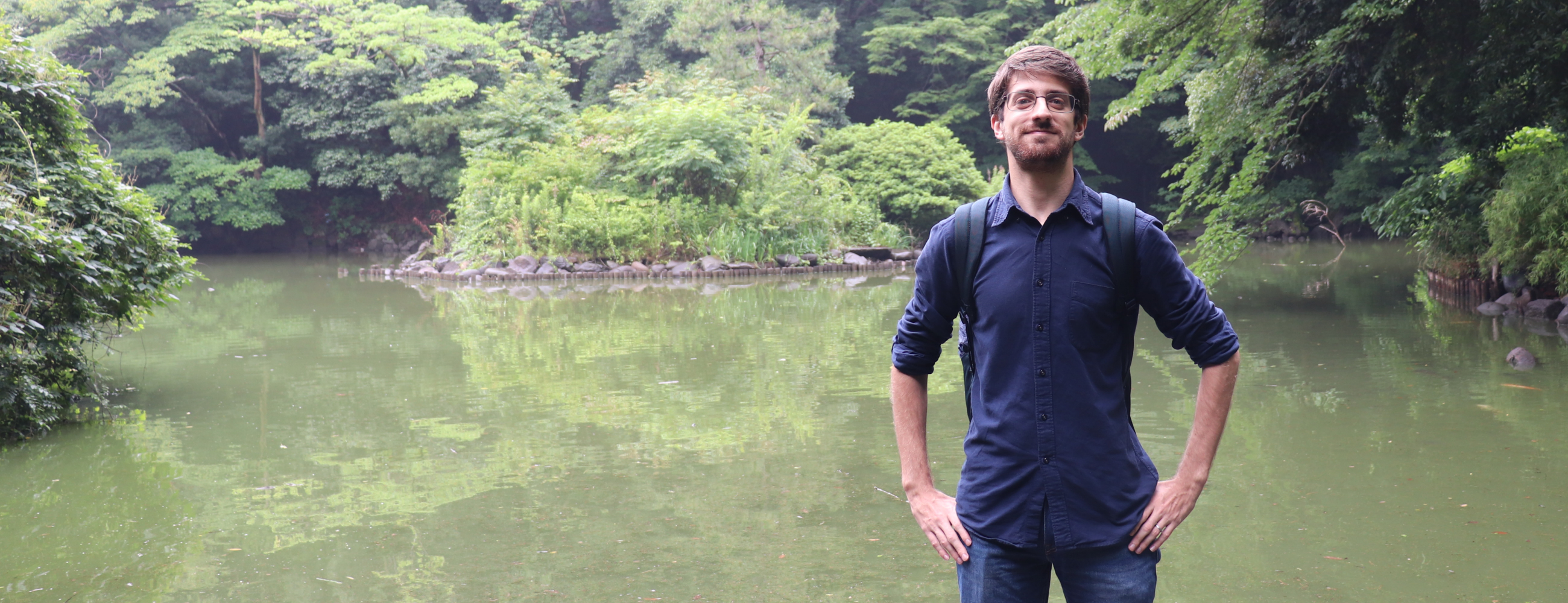 Student standing in a green area in front of a pond