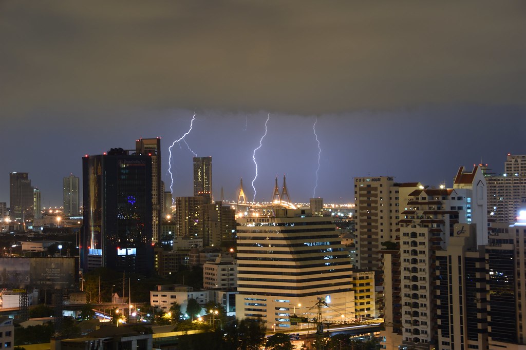 A dark sky above a night time cityscape. Lightning bolts in the distance.