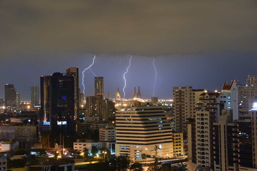 A dark sky above a night time cityscape. Lightning bolts in the distance.