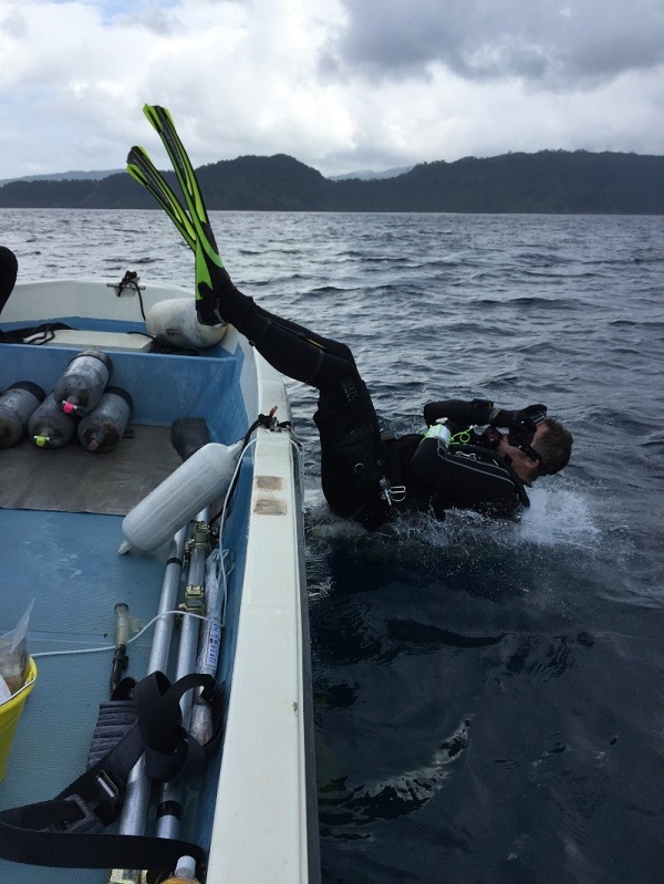 A SUCBA diver enters the ocean by falling backwards off the side of a small boat.