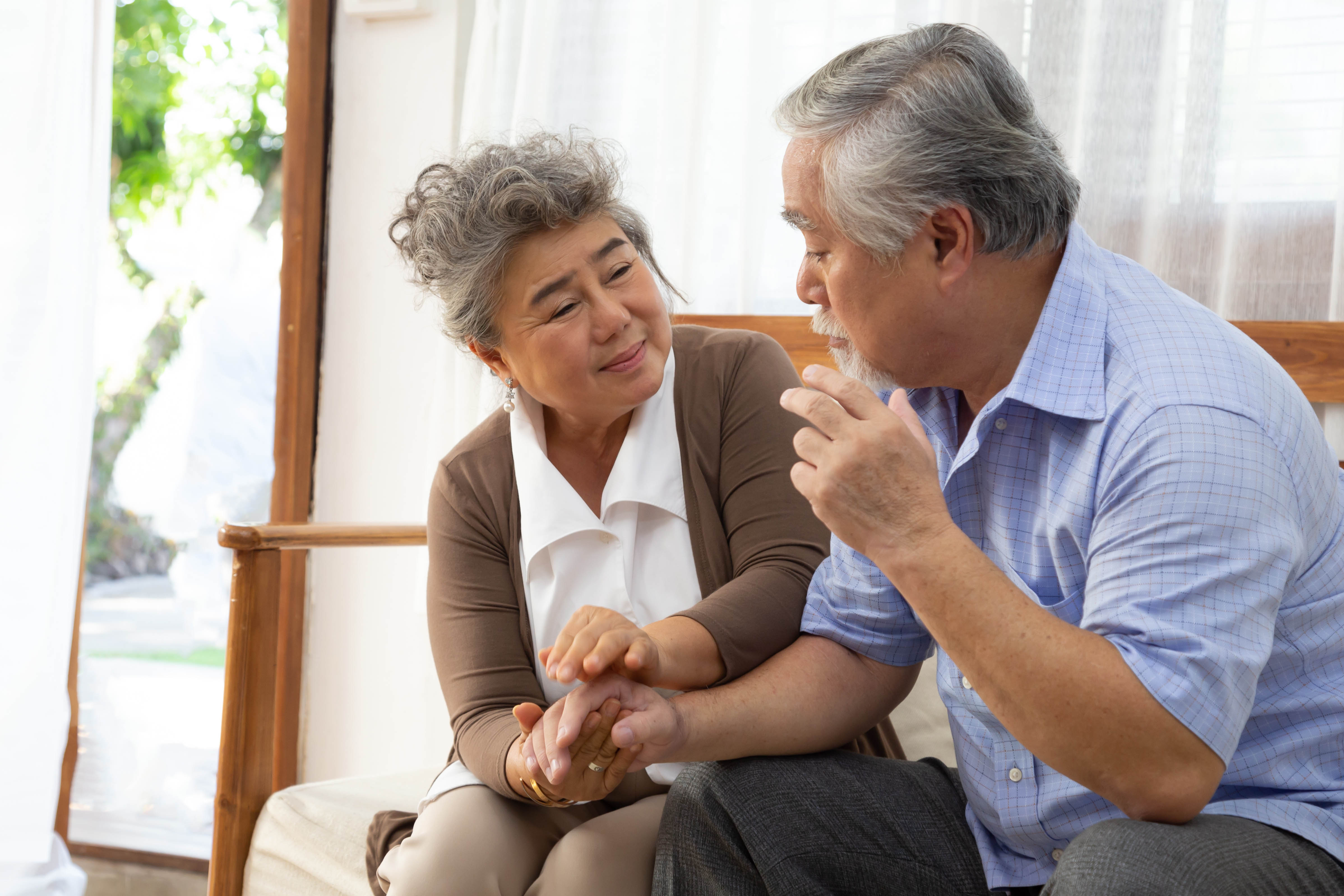 Elderly man and woman holding hands and sitting on a couch .