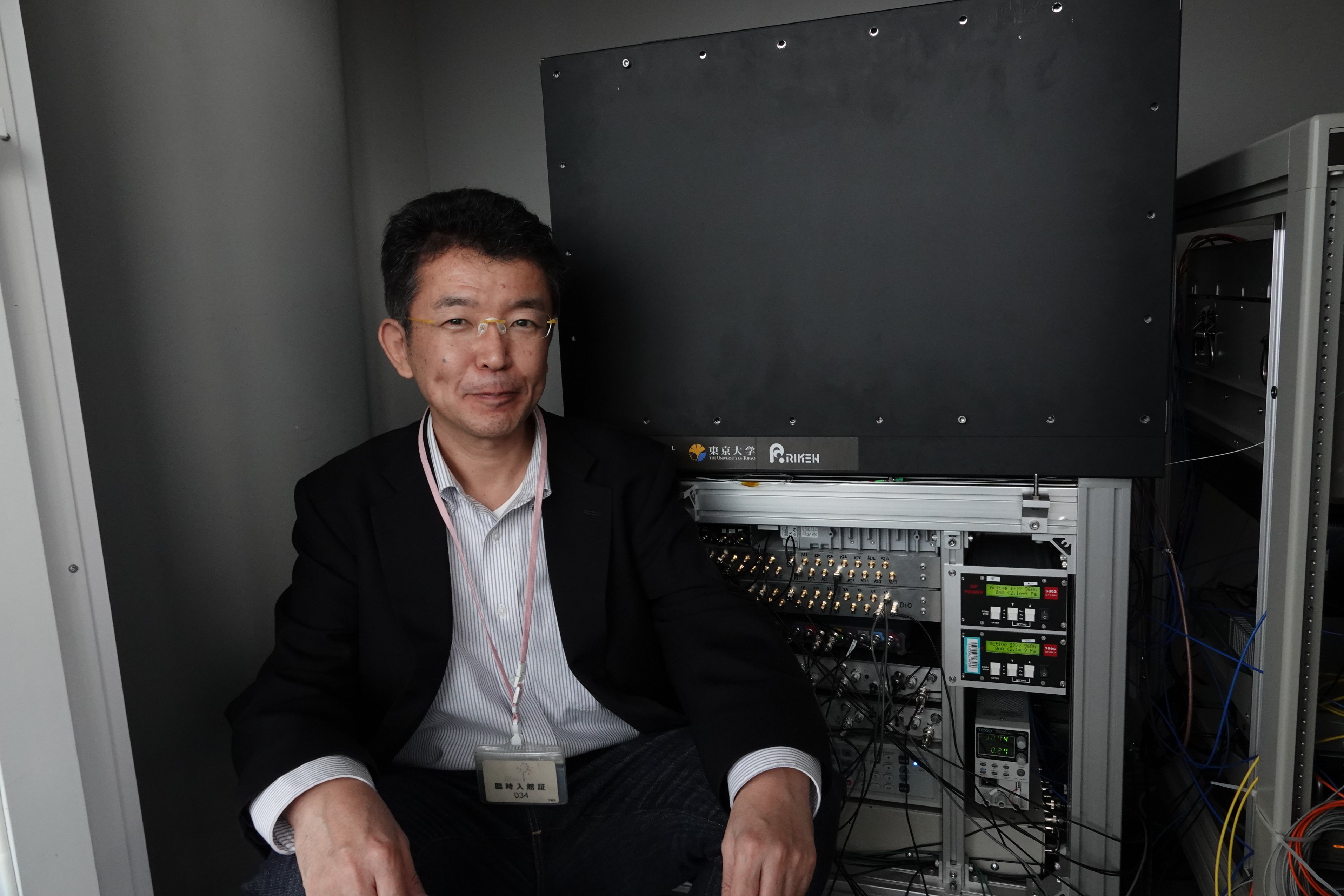 A man sitting next to a grey box with wires coming out of it.