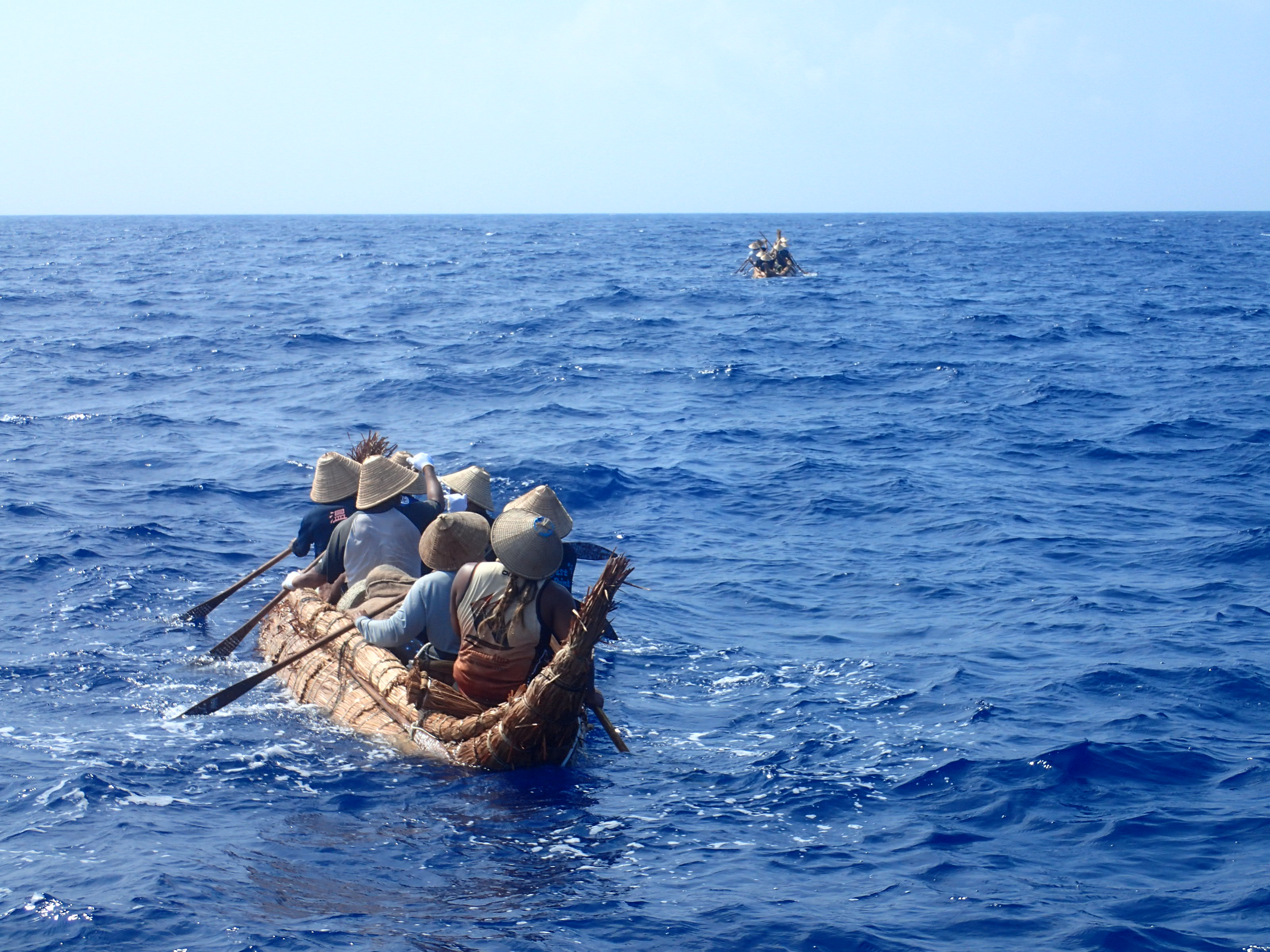 A small boat on the ocean, several people in pointed hats are paddling it