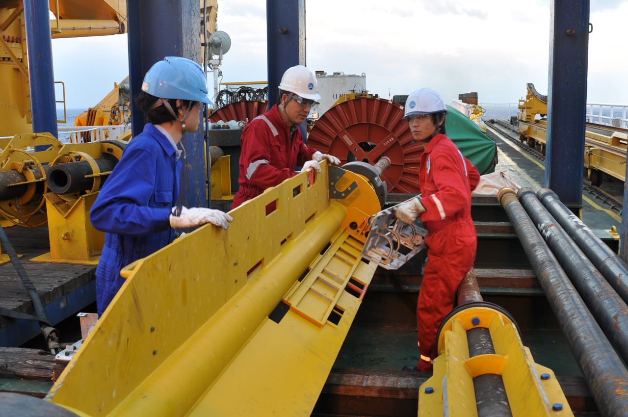 Three men in hard hats holding a large yellow metal object