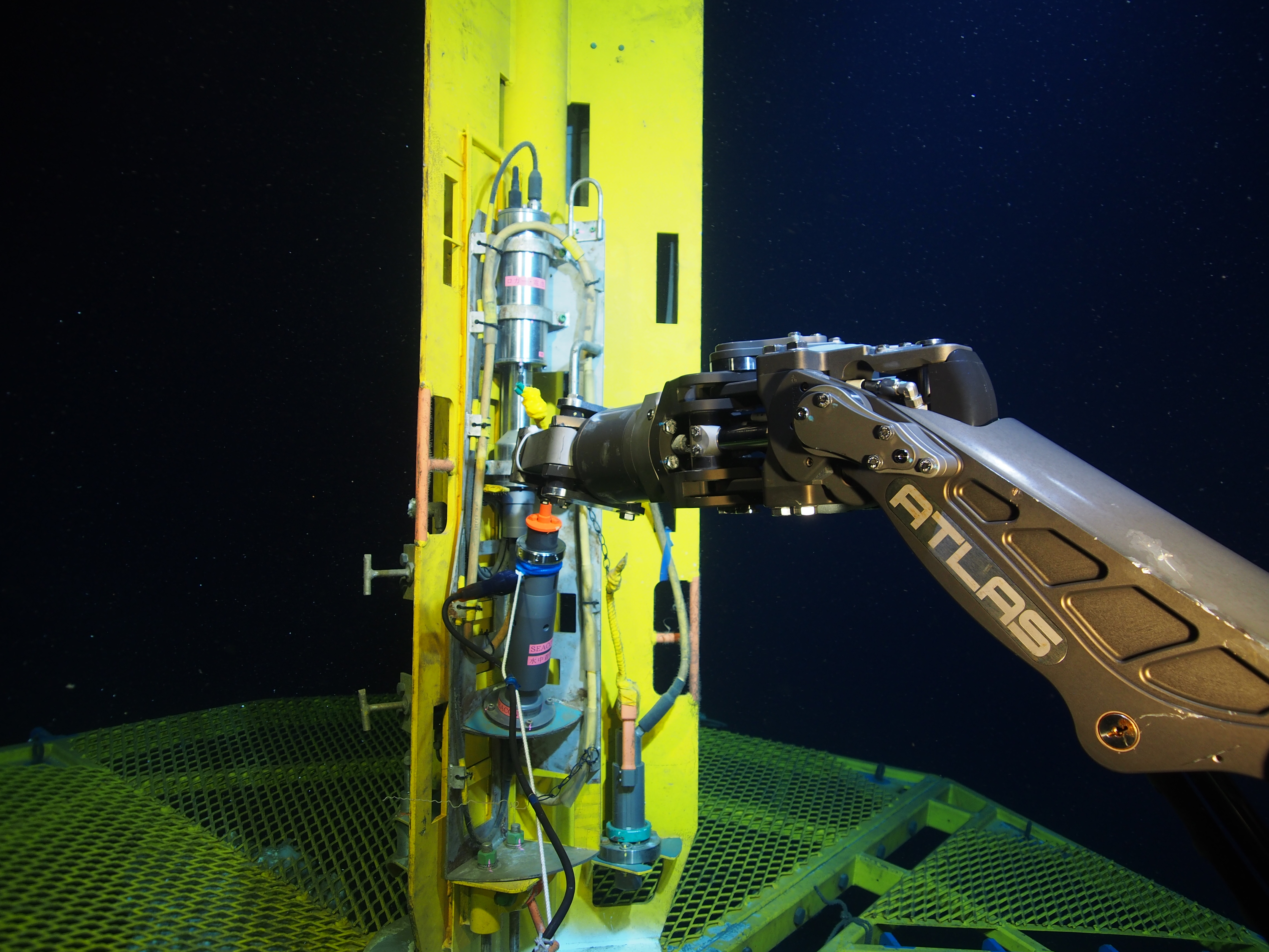 A dark blue background, a vertically orientated yellow metal shape in the center is held by a grey robot arm from the right.