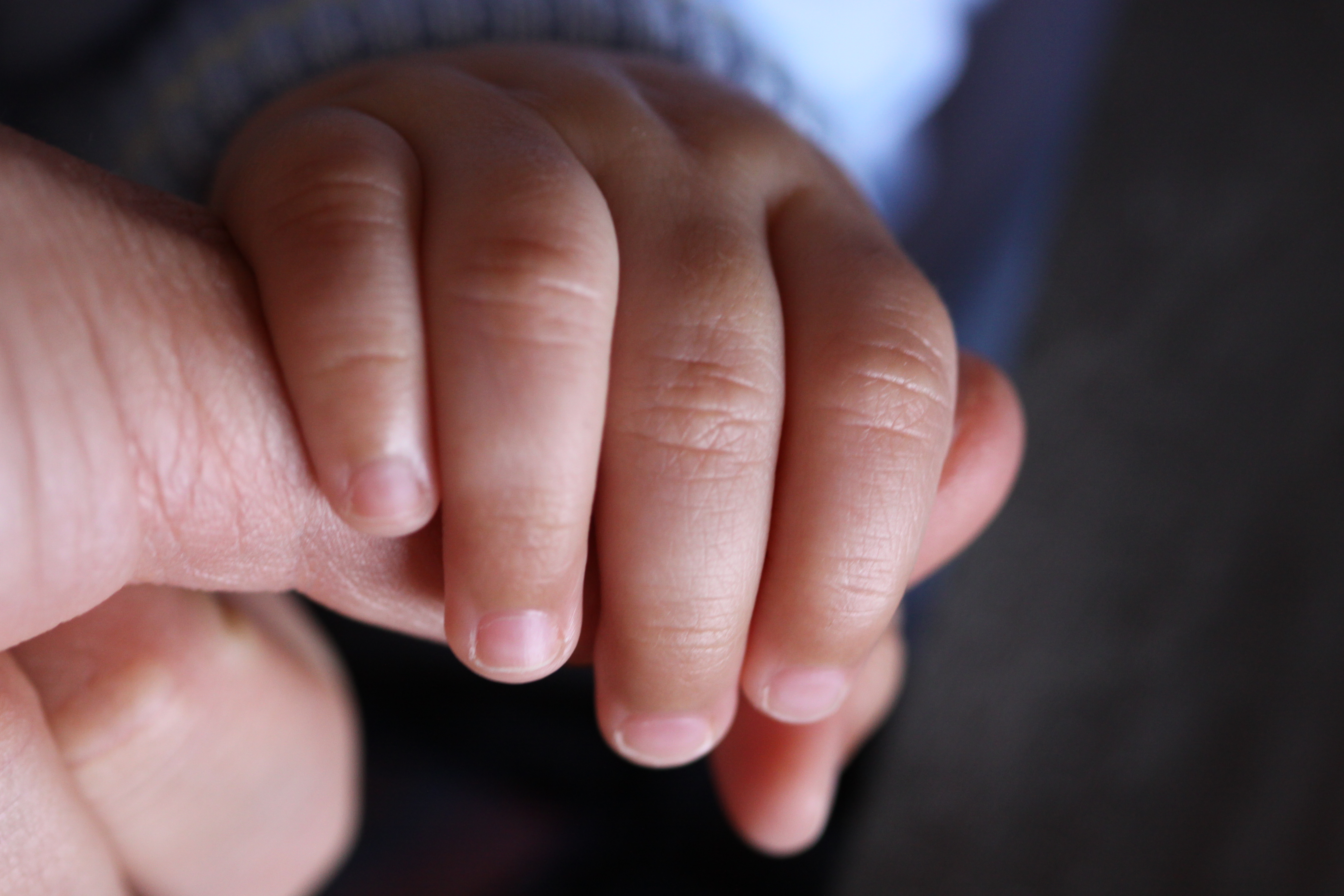 A baby's hand gripping an adult thumb