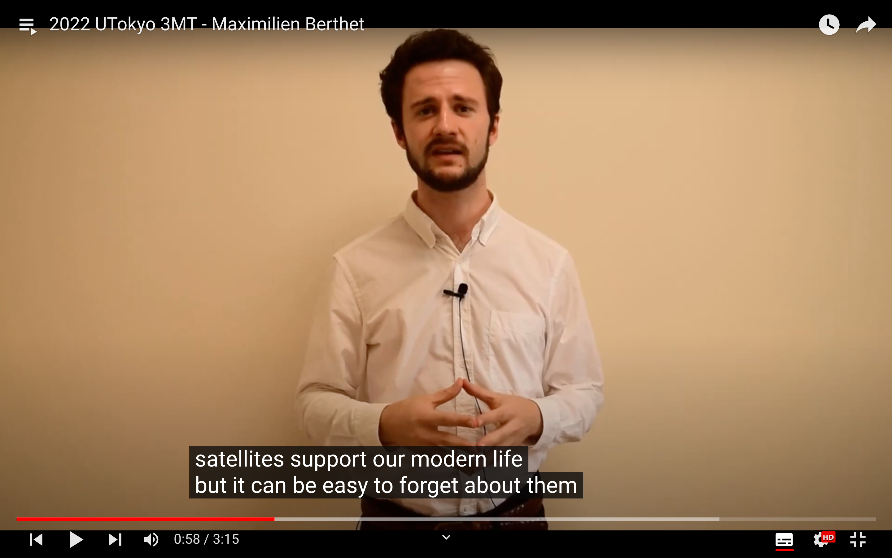 Maximilien Berthet stands in front of a white wall as he delivers his 3MT presentation, in a screenshot from his YouTube video.