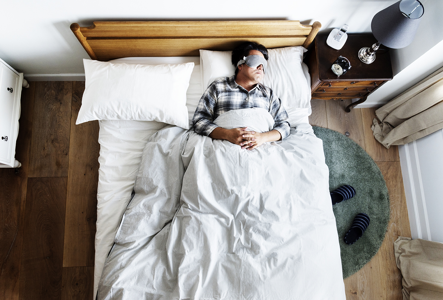 Japanese man lying sleeping in bed while wearing an eye-mask.