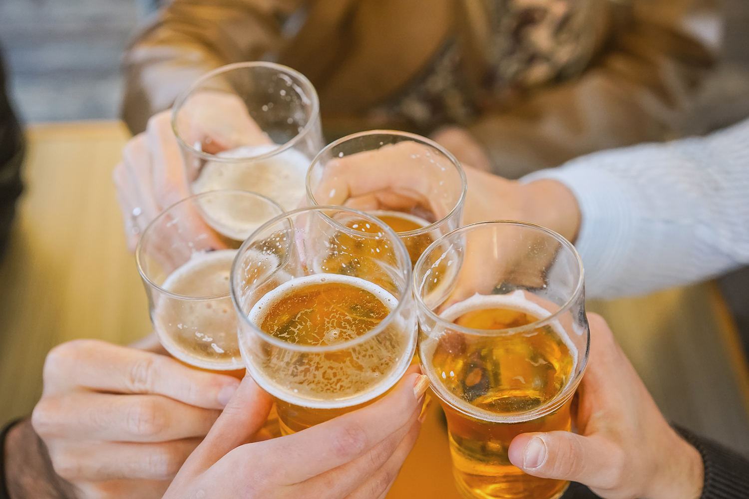 A photo of a group of hands holding beer filled glasses in a circle.