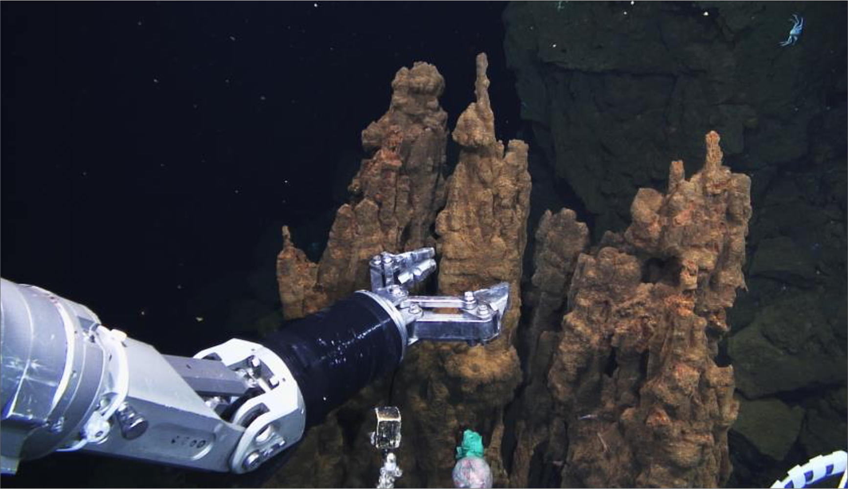 Undersea photo of a robotic arm moving to grasp the vent being extracted.