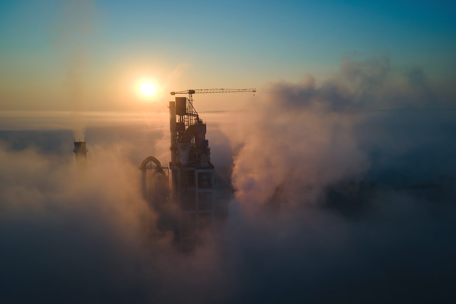 Cement factory tower emerging from clouds, in front of a sunset 