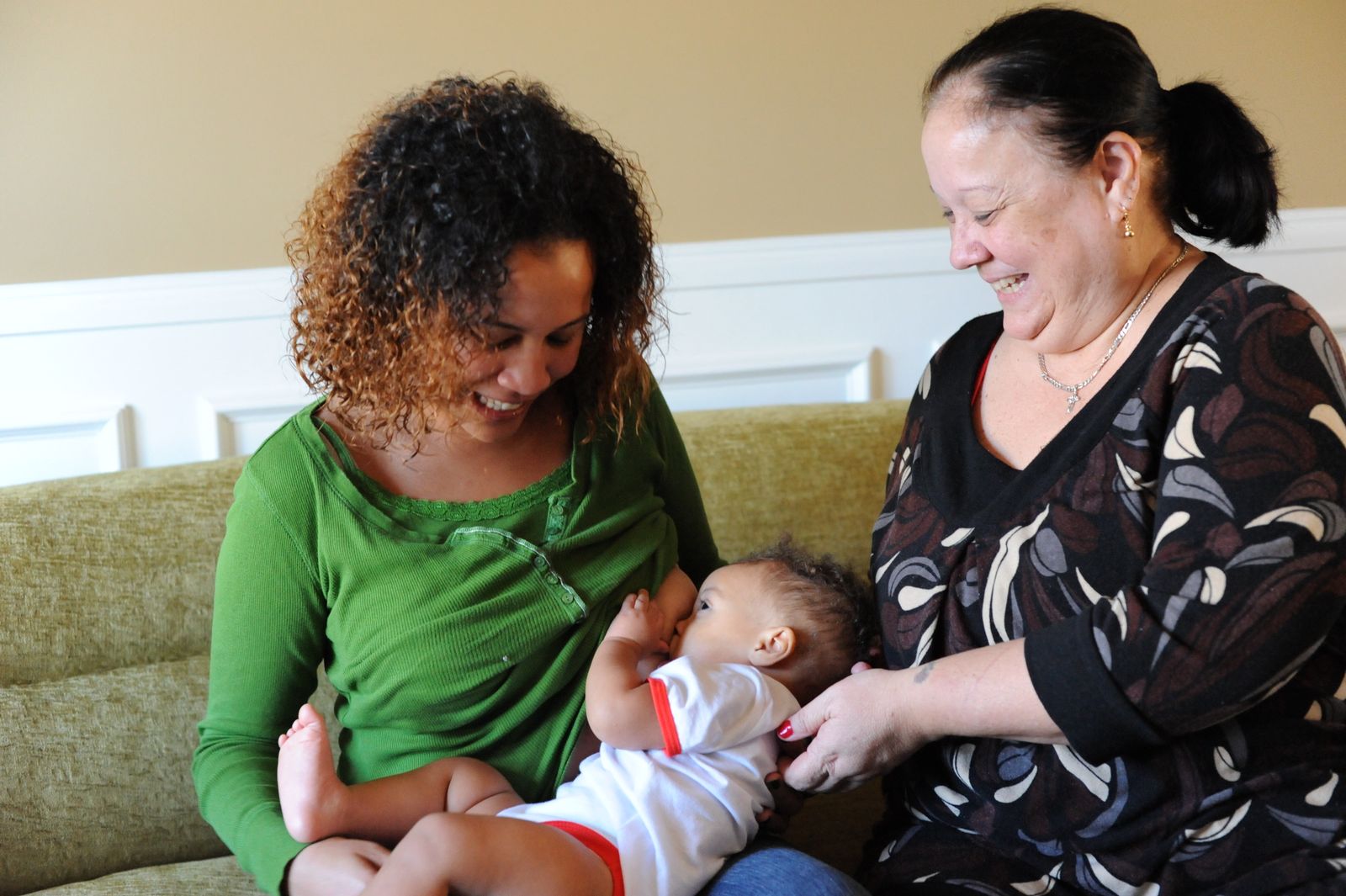 Young woman breastfeeding while an older woman offers support, both smiling.