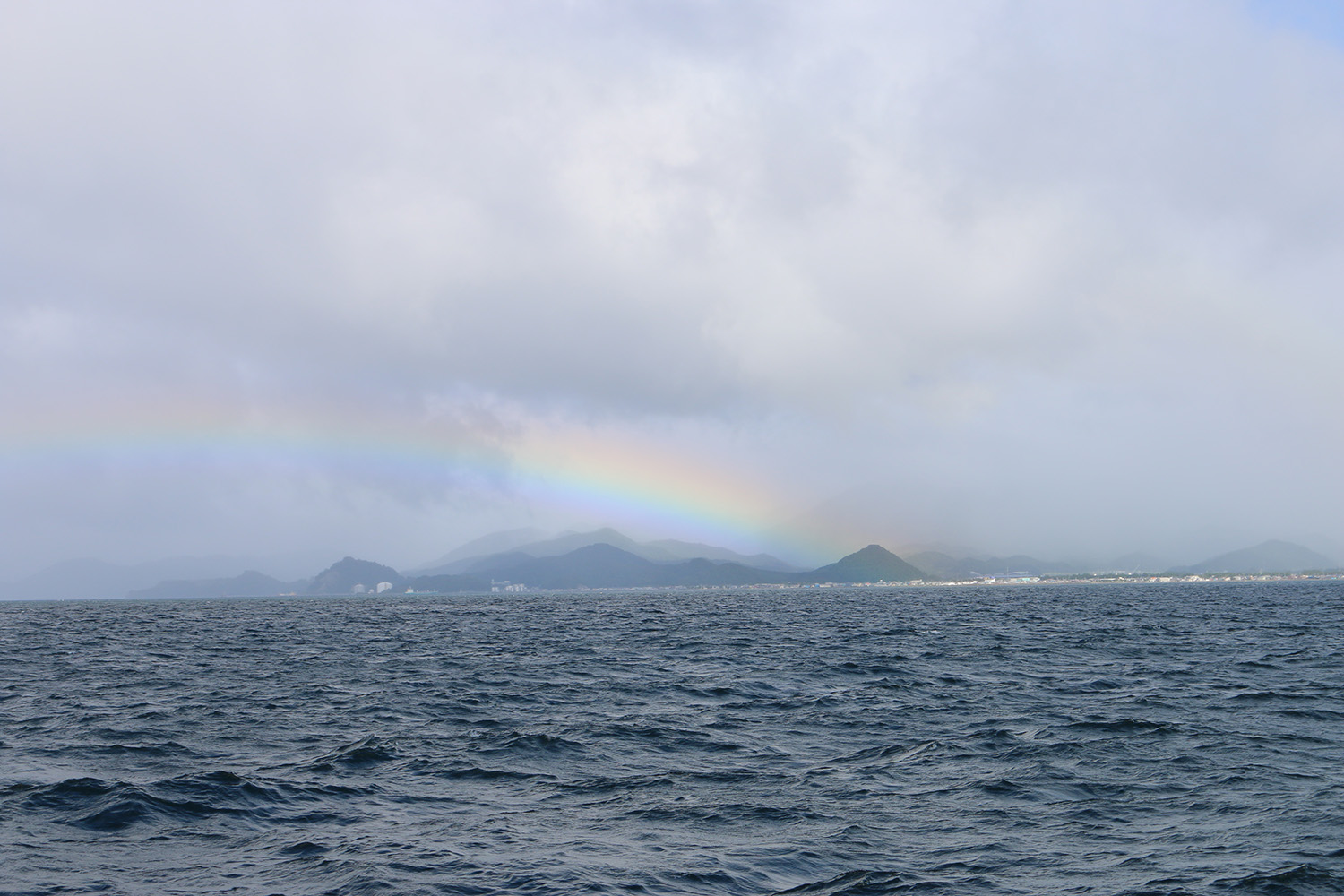 Photo of north Japan's Aomori coastline, from the sea with a rainbow over the land.