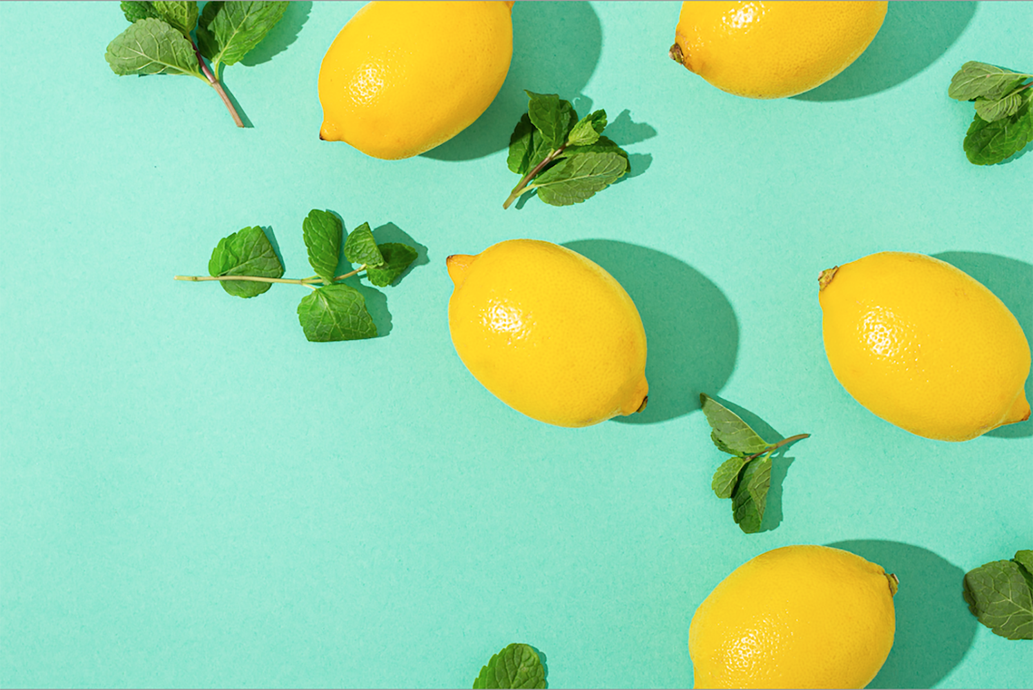 Photograph of lemons and mint leaves against a bright light turquoise background.