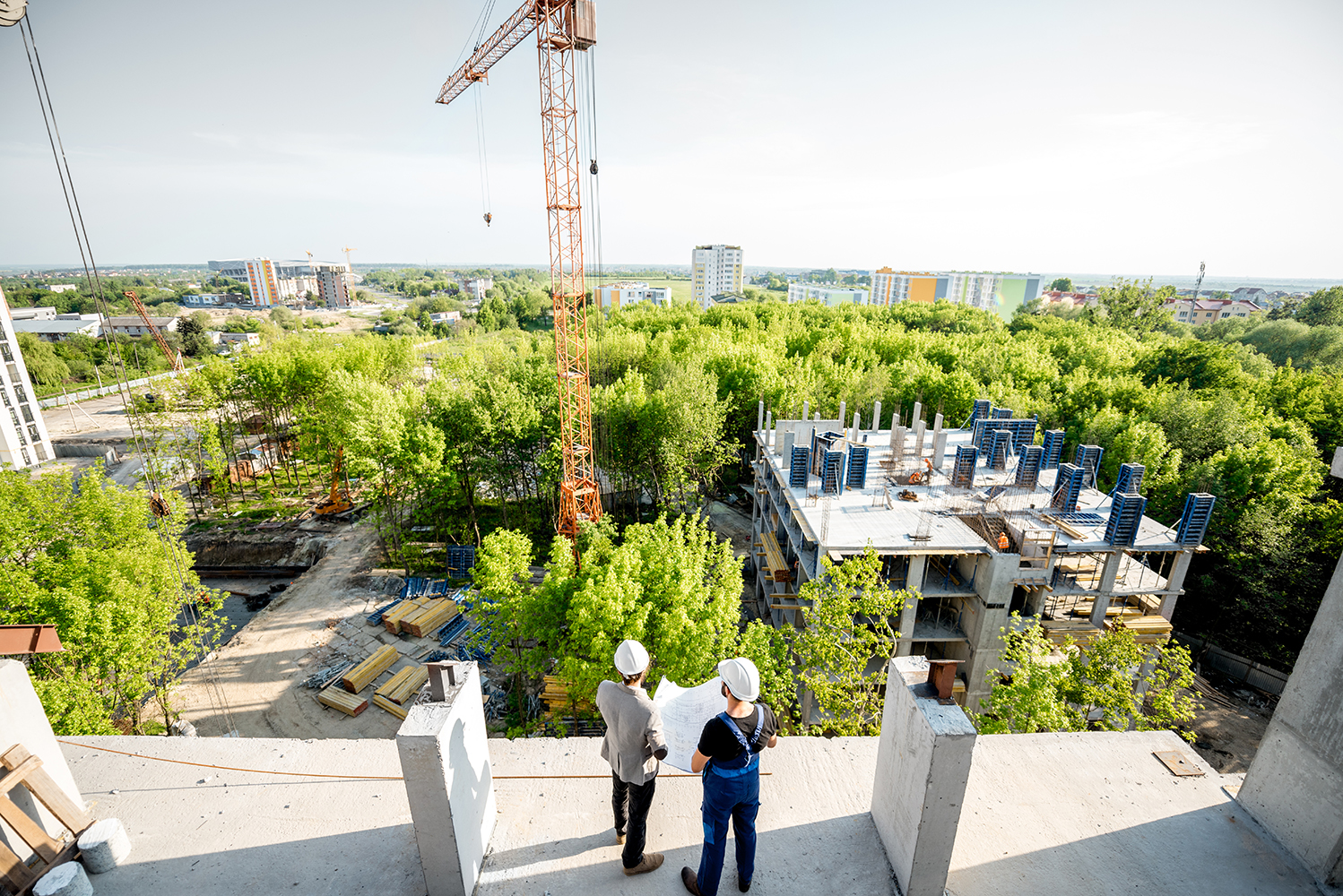 Photograph of construction workers standing on an unfinishes building, looking out over a construction project in a forest.