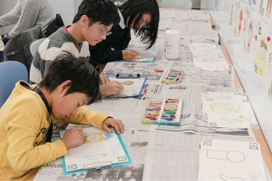 「デジタルからくり装置づくり ワークショップ」で子どもたちが机に向かって絵を描いている様子