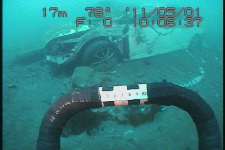 The remains of an automobile found at the depth of 17 meters underwater in Otsuchi Bay. The black bar in the foreground is the bumper of the ROV.