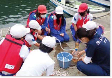 漁港でグラスに入った海水を濾過している小学生と沿岸センターの職員