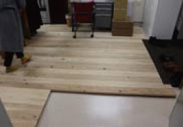 木材を敷き詰めた床にオフィスデスクなどが置かれた部屋と靴下で歩く人