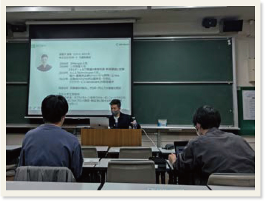 自己紹介が映っている教壇中央のスクリーン手前に座る渡慶次さんと向かい合う参加者
