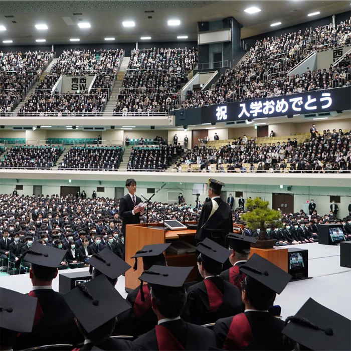 壇上側から見た総長と入学生総代。観客席のディスプレイに「祝　入学おめでとう」の表示がある