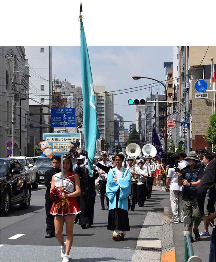 「七大戦パレード」と書かれたプラカードを持って歩く応援部のメンバー