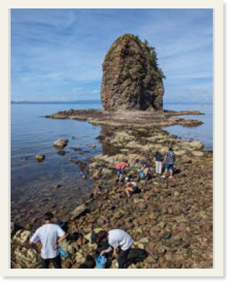 裸島の手前の磯浜海岸でバケツを置いて生物を探す学生