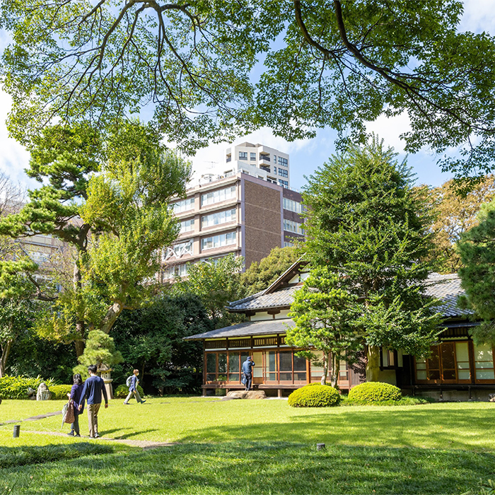 木々や芝で覆われた庭園を歩く人や奥の和風建築を見学する人