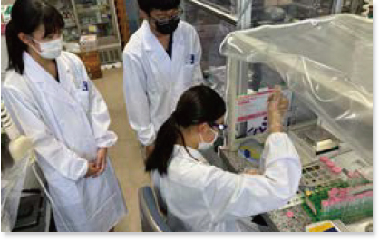 研究室で白衣を着た3人の参加者。そのうち1人が座ってピペットを持っている様子