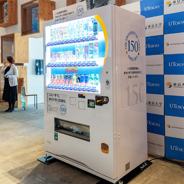 「この自動販売機は、東京大学150周年を寄付で、応援しています。」と書かれたラベルが貼られた白い自動販売機