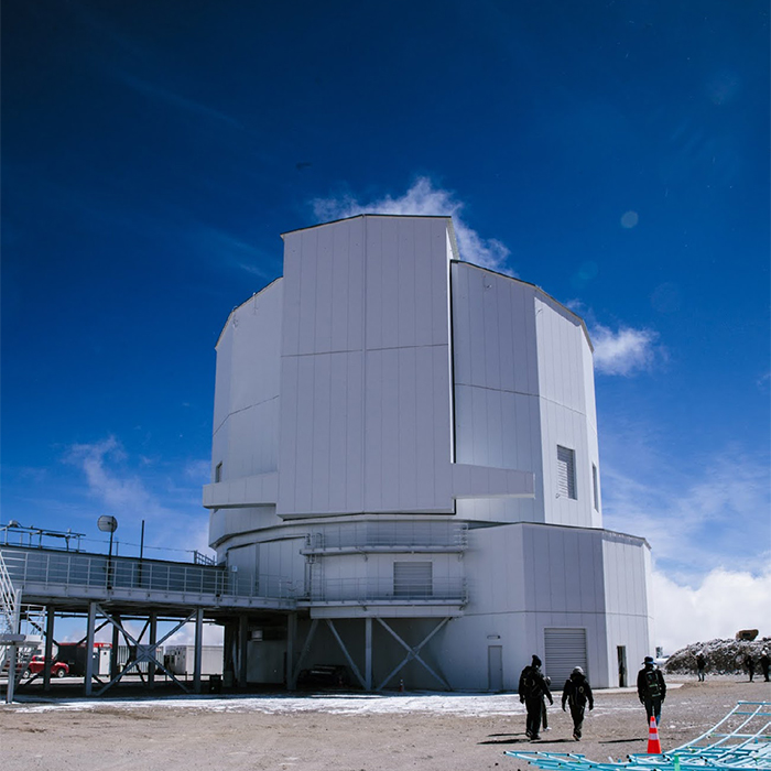 青空の下に雪が残っている巨大な望遠鏡の建物、およびその奥に向かって歩く人々
