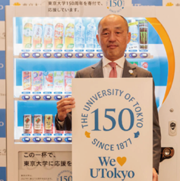 自動販売機の前で「We♥UTokyo」と書かれたパネルを持つ男性