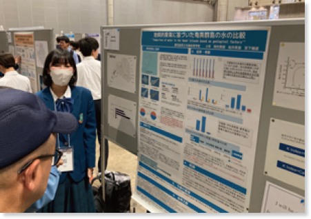 展示会場のポスターを見ている人に説明する生徒