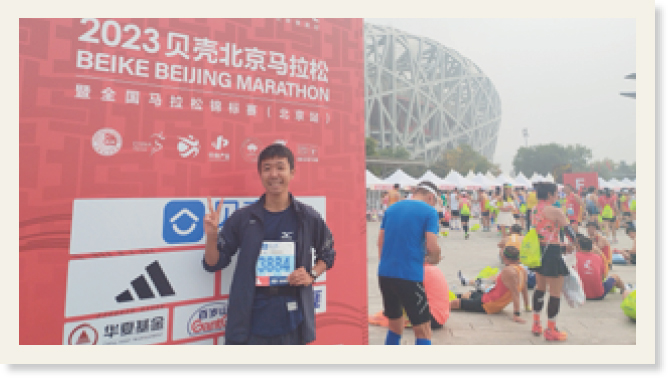 北京国家体育場をバックに「BEIKE BEIJING MARATHON」と書かれたボードの前でピースサインをする小原さん
