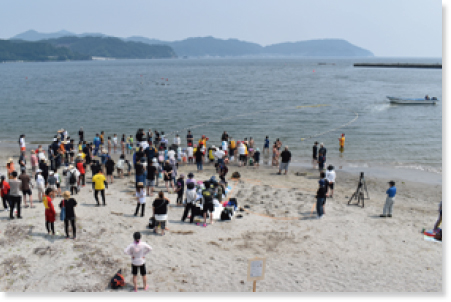 浜辺に集まって地引き網を持っている参加者や見学者の様子
