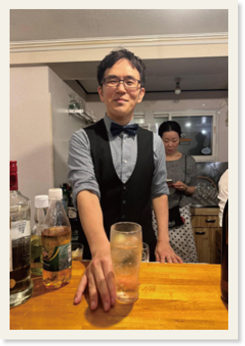 バーテンダーの服装で氷が入ったカクテルを差し出す長谷川さん